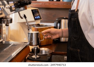 Barista frothing milk with steam wand standing in bar Stainless steel pitcher under steam wand with foam forming, Close-up of barista hand, Professional coffee preparation in  small business cafe - Powered by Shutterstock