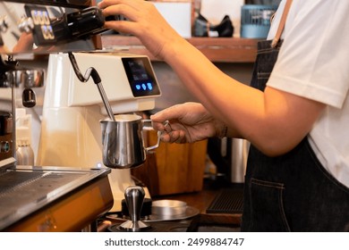 Barista frothing milk with steam wand standing in bar Stainless steel pitcher under steam wand with foam forming, Close-up of barista hand, Professional coffee preparation in  small business cafe - Powered by Shutterstock