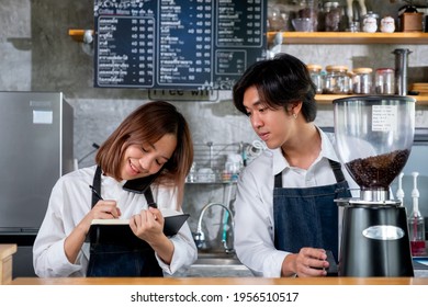 Barista Girl Or Coffee Maker Answer Mobile Phone Also Record The Order Detail Into Notebook While Her Co-worker Is Working With Machine. Concept Of Good Teamwork Support Small Business System.