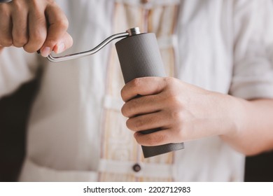 Barista Is Grinding Coffee Beans With Manual Stainless Steel Grinder To Make Black Coffee Machine, Brewing Equipment Or Coffee Drip Set Dripper On A Wooden Table In The Kitchen At Home In The Morning