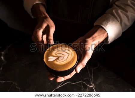 Barista hands holding cup of Latte art coffee in coffee shop