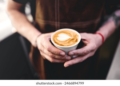 Barista holding cappuccino, standing by counter. Bartender in apron preparing coffee drink. - Powered by Shutterstock