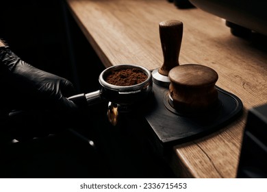 barista holding portafilter with grinded coffee, tamper, wooden table, cafe, alternative brew - Shutterstock ID 2336715453