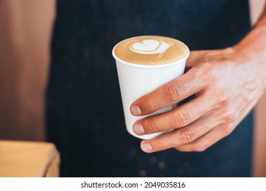 The Barista Holds The Finished Coffee In His Hand In A Paper Cup With A Heart Pattern Made With Cream