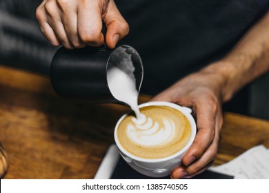 Barista making cappuccino with latte art. Close up of bartender hands prepares a coffee with a draw on foam. Specialty coffee - Powered by Shutterstock