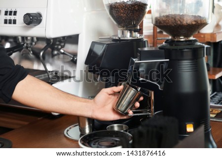Barista with metal cup using coffee grinding machine in cafe, closeup