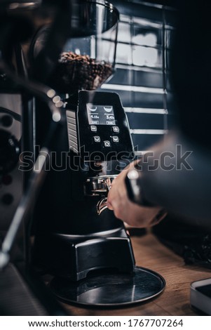 Barista picks up ground coffee from a coffee grinder to a holder - making espresso in a cafe