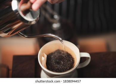 The barista poured hot water from the kettle over the coffee powder to extract the freshly brewed coffee in the coffee shop.