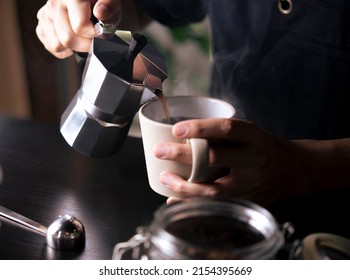 Barista pouring coffee from moka pot coffee maker to a coffee cup. Hand holding Italian classic moka pot pouring coffee. - Shutterstock ID 2154395669