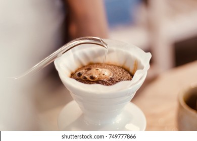 barista pouring hot water on rough brown bubbles coffee through drip filter, home brewing process - Shutterstock ID 749777866