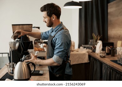 Barista pours coffee beans into the coffee machine tank for grinding standing behind counter