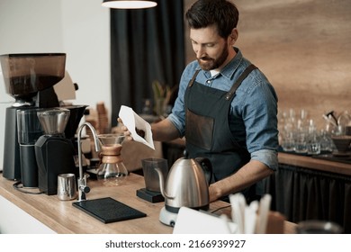 Barista pours coffee beans into the coffee machine tank for grinding standing behind counter