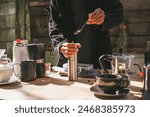 The barista is preparing a fresh brew by pouring roasted Arabica beans into a manual stainless steel grinder at a rustic outdoor café setup, delicious and aromatic coffee experience