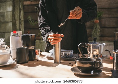 The barista is preparing a fresh brew by pouring roasted Arabica beans into a manual stainless steel grinder at a rustic outdoor café setup, delicious and aromatic coffee experience - Powered by Shutterstock