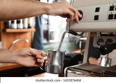 Barista steaming milk in metal jug with coffee machine wand at bar counter, closeup - Powered by Shutterstock