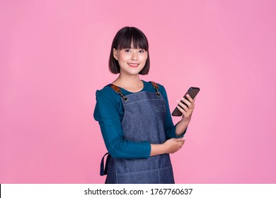 Barista waitress using mobile smartphone café shop Asian woman confident independent start up small business owner employee worker busy entrepreneur occupation wearing apron pink isolated background - Powered by Shutterstock