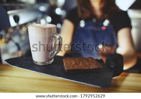 Barista wearing medical latex black gloves, making pink matcha latte with milk. Bartender preparing tasty drink and brownie cake.Blurred image,selective focus