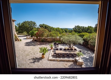 Barjac, France - July 24th 2022 : View On A Private Provençal Garden In The South Of France From A Balcony Of The Large Stone Villa With Gravel, Olive Trees, Shrubs And A Terrace With Wooden Tables