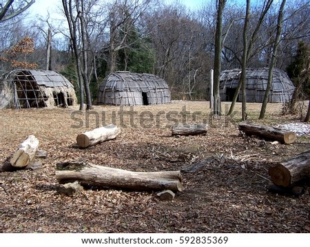 Bark-covered wigwams seen beyond a fire circle at a reconstructed Native American village in Maryland, home to the Nanticoke, Shawnee, Piscataway, Lenape, Tuscarora, and Susquehannock nations.