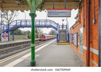 Barkingside, Ilford, Essex, UK - April 6, 2018:  Shot Of The Platform With A Passenger On The Footbridge Of Tube Station With Train Departing.