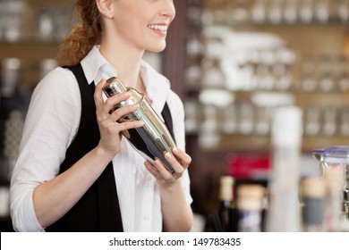 Barmaid shaking a cocktail shaker as she stands behind the bar mixing a drink for a client - Powered by Shutterstock