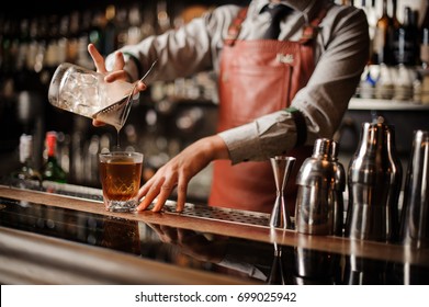 Barman In Bar Interior Making Alcohol Cocktail. Professional Bartender Pours Drink With A Strainer