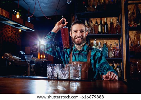 A barman with bottle of alcohol smiles laughing at the bar.