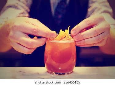 Barman is decorating cocktail with lemon zest, toned image