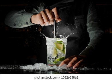 Barman hand squeezing fresh juice from lime in the glass making the Caipirinha cocktail on the bar counter - Shutterstock ID 1032633862