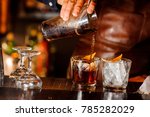 Barman pouring fresh alcoholic drink into the glasses with ice cubes on the bar counter