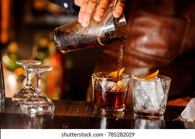 Barman pouring fresh alcoholic drink into the glasses with ice cubes on the bar counter - Shutterstock ID 785282029