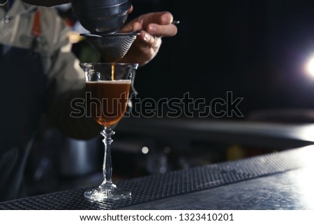 Barman pouring martini espresso cocktail into glass at counter, closeup. Space for text