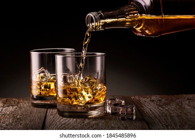 Barman pouring whiskey from bottle into the cristyl glass for whiskey with ice cubes on black background. Glass of scotch whiskey and ice on black background - Powered by Shutterstock