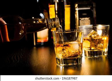 Barman Pouring Whiskey In Front Of Bottles On Wood Table, Focus On Top Of Bottle