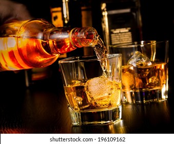 barman pouring whiskey in front of whiskey glass and bottles on wood table