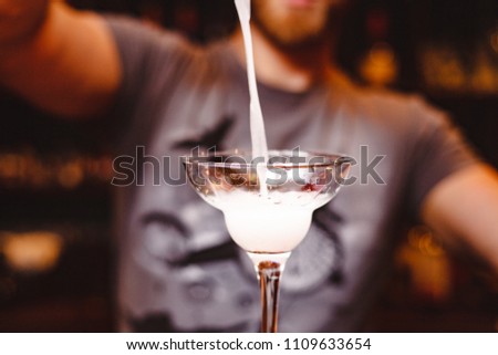 The barman pours a cocktail with a glass of Margarita