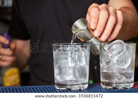 The barman pours gin into a glass with ice