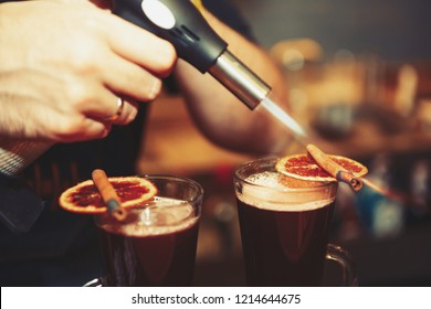 Barman prepares glintwein cocktail in cold autumn day. Bartender burns cinnamon sticks for mulled wine with gas torch in bar - Powered by Shutterstock