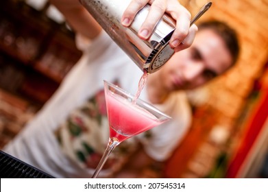 Barman Preparing And Pouring Cosmopolitan Alcoholic Cocktail Drink At Bar. Alcoholic Drink With Vodka, Triple Sec, Cranberry Juice And Lemon Juice