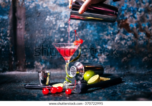 barman preparing and pouring\
red cocktail in martini class. cosmopolitan cocktail on metal\
background