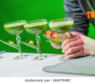 Barman presents his green cocktails while making an alcoholic or non-alcoholic refreshing drink for a group of girls