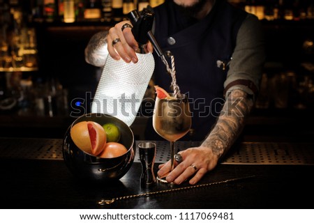 Barman with tattoo pouring cold soda into the copper cocktail glass with summer cocktail, fruit and straw