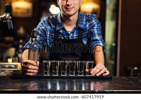 Barman at work pouring hard spirit into glasses and preparing cocktails in detail