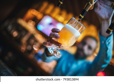 Barmen or brewer filling glass with beer. Barmen is pouring lager beer to glass from  beer taps. Bar or night club interior - Powered by Shutterstock