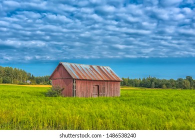 a barn in the middle of a summer field and clouds in the sky