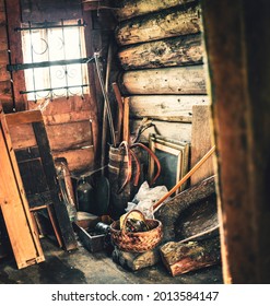 A barn in an old wooden log house full of antique agricultural rustic items made of metal, wood. Openwork forged lattice on a small window. The cracks are plugged with moss. Warm colors, wide angle.
