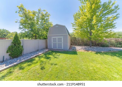 Barn tool shed at the corner of a fenced backyard against the trees and shrubs at the back