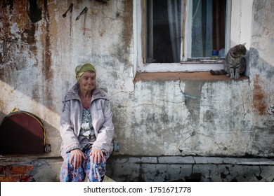 Barnaul, Russia-may 12, 2020. An old woman in a headscarf sits against the wall of an old house with a cat