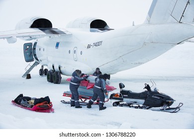 Barneo Drifting Camp, North Pole - April 10, 2015: Airplane Stands On Ice. Workers In Warm Uniform Loading Luggage Snowmobile. Snow On Arctic Ice. 