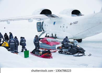 Barneo Drifting Camp, North Pole - April 10, 2015: Airplane Stands On Ice. Workers In Warm Uniform Loading Luggage Snowmobile. Snow On Arctic Ice. 